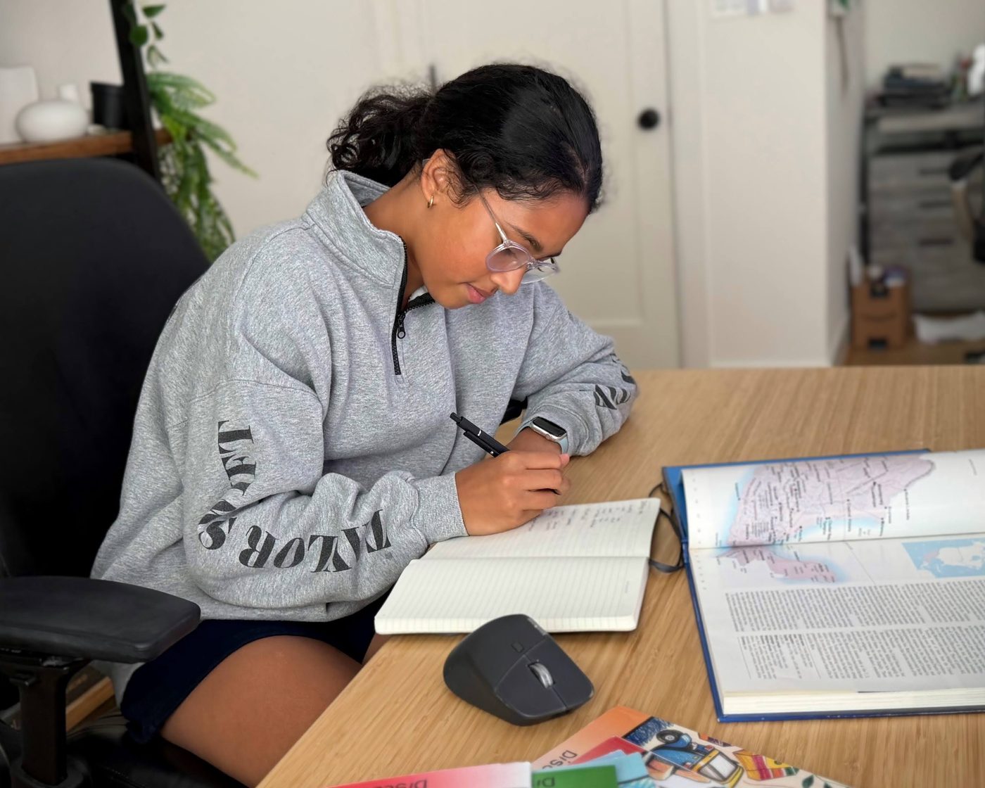 Me at my desk, researching a country and taking notes beside an atlas